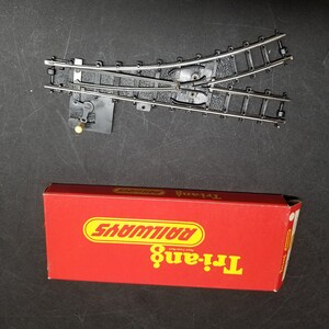 May include: A red box with the text "Tri-ang Railways" in yellow letters. The box contains a model train track switch.