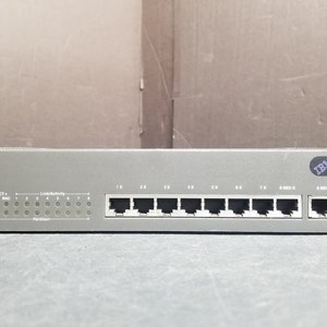 Könnte beinhalten: Ein silberner IBM 8222-008 Netzwerk-Switch mit acht RJ-45-Ports und einem MDI-Port. Der Switch hat ein Etikett mit dem Text "Link/Activity" und "Partition".