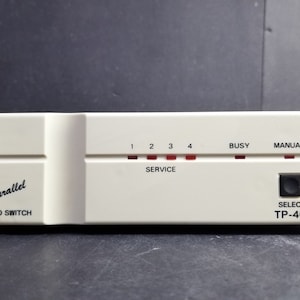 May include: A cream-coloured Parallel Auto Switch, model TP-401, with red indicator lights labelled 1, 2, 3, 4, Busy, and Manual. It has a black Select button. The device is rectangular.