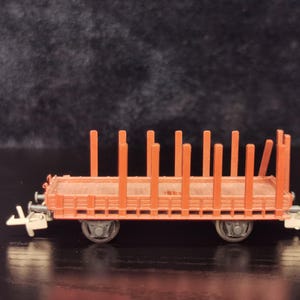 May include: A red toy train carriage with a wooden cargo bed and vertical wooden posts. The carriage has two sets of wheels and a metal frame.