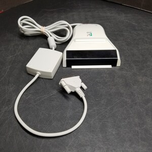 Peut inclure: Un scanner de code-barres blanc avec une fenêtre noire, un adaptateur secteur blanc et un câble série blanc avec un connecteur 9 broches.