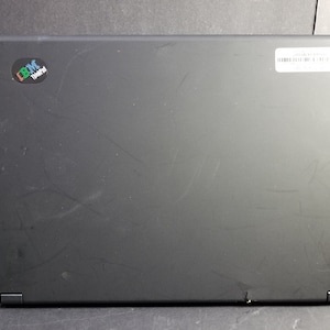 Könnte beinhalten: Schwarzer Laptop mit einem kleinen Aufkleber mit der Aufschrift "IBM ThinkPad" auf dem Deckel. Der Laptop hat ein paar Kratzer auf dem Deckel.