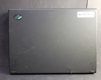 Puede incluir: Ordenador portátil negro con una pequeña pegatina que dice "IBM ThinkPad" en la tapa. El portátil tiene algunos arañazos en la tapa.
