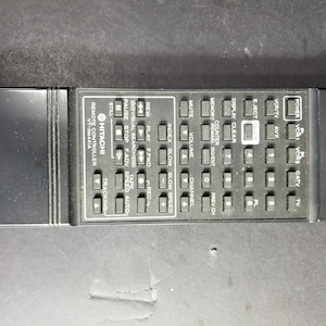 May include: Black remote control with a variety of buttons, including power, VCR, TV, channel, volume, play, rewind, fast forward, record, and more. The remote control is labeled "HITACHI" and "REMOTE CONTROLLER VT-RM441A".