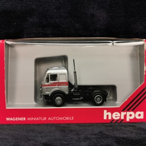 May include: A silver and black model truck in a red box with the text "WAGNER MINIATUR AUTOMOBILE" and "herpa" on the front.