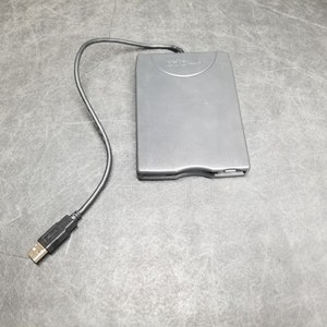 Peut inclure: Un lecteur de disquette externe noir avec un câble USB. Le lecteur porte une étiquette indiquant "Iomega".