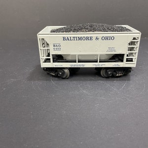 May include: A white model train car with black wheels and a gray metal frame. The car is labeled "Baltimore & Ohio" and "B&O 6453". The car is filled with black coal.