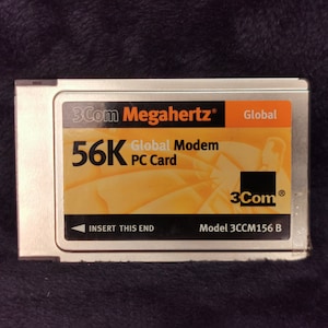 May include: A silver 3Com 56K Global Modem PC Card. The card has the 3Com and Megahertz logos, with the text "Global Modem PC Card" and "56K". The card also has the text "Insert this end" and model number 3CCM156 B.