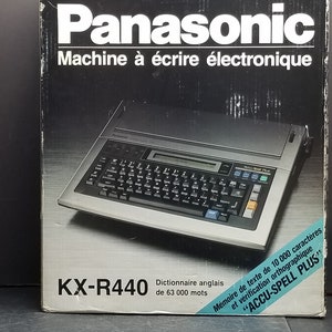 Puede incluir: Una máquina de escribir electrónica Panasonic KX-R440 en su caja original. La caja presenta el logotipo de Panasonic y el texto "Machine à écrire électronique". La máquina de escribir tiene un teclado y una pequeña pantalla.