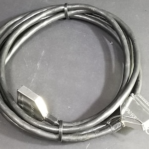 Könnte beinhalten: Ein schwarzes Kabel mit zwei silbernen Steckern. Ein Stecker ist mit "AMPHENOL" und der andere mit "AMP" beschriftet, beide Stecker haben mehrere Pins.