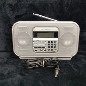 Könnte beinhalten: Ein silbernes Radio mit einem schwarzen Stromkabel und dem Wort "CENTRIOS" auf der Vorderseite.