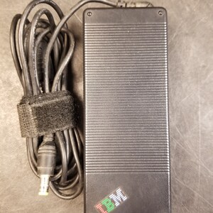 May include: A black laptop power adapter with a black power cord and a black velcro strap. The adapter has a black and green IBM logo.