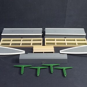 Puede incluir: Un conjunto de estación de tren modelo con plataformas grises, ventanas beige y vigas de soporte verdes. El conjunto incluye dos plataformas, dos secciones de ventanas, dos piezas de techo curvadas, un banco de plataforma y cinco vigas de soporte.