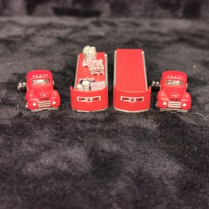 May include: Three red toy trucks with flatbeds. The trucks have black wheels and are hauling various cargo. The flatbeds have the text "UPS" printed on them.