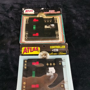 May include: Two model train controllers in their original packaging. The top controller is labeled "#220 Controller" and the bottom controller is labeled "#220 Custom-Line Controller". Both controllers are black with red and green buttons.