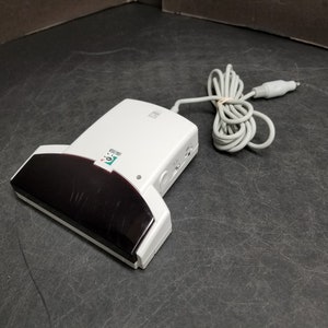 Peut inclure: Un lecteur de cartes blanc et noir avec un logo vert qui dit "Logitech". Le lecteur a un scanner noir et un cordon blanc.