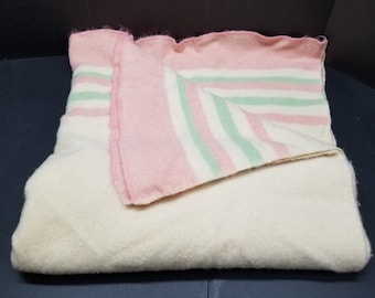 Op de afbeelding: Een wit wollen deken met roze en groene strepen. Het deken is dubbelgevouwen en de strepen zijn zichtbaar op de bovenste helft.