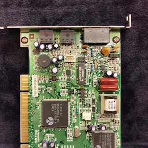 Könnte beinhalten: Eine grüne Leiterplatte mit verschiedenen elektronischen Bauteilen, darunter Chips, Kondensatoren und Widerstände. Die Platine hat einen schwarzen Stecker in der oberen rechten Ecke und ein Etikett mit der Aufschrift "11235-14 @ROCKWELL 98 9910 B 77160.9 KOREA".