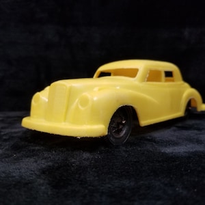 Puede incluir: Un coche de juguete de plástico amarillo con un diseño detallado. El coche tiene un parabrisas negro y ruedas negras.