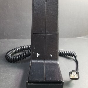 Könnte beinhalten: Schwarze Telefonbasis mit einem Spiralkabel und einem RJ-45-Stecker. Die Basis hat zwei Tasten, eine mit einem Lautsprechersymbol und die andere mit einem Blitzsymbol.