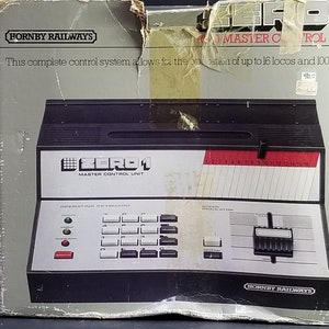 Könnte beinhalten: Eine Schachtel für eine Hornby Railways Zero 1 Master Control Unit für Modelleisenbahnen. Die Schachtel ist grau und weiß mit dem Text "Hornby Railways" und "Zero 1 Master Control Unit" bedruckt. Die Schachtel zeigt eine schwarze und silberne Steuereinheit mit einer Tastatur und einem Display.