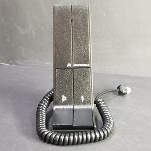 Könnte beinhalten: Eine schwarze Motorola Zweiwegefunk-Ladestation mit einem Spiralkabel.