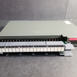 May include: A gray electronic component with a rectangular shape and a series of connectors. A detachable gray module with white rectangular inserts is in front of the main unit. The component has a label with text.