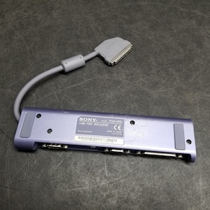 Puede incluir: Un replicador de puerto de enlace Sony morado, modelo PS2A-LPR5, con un cable gris. El dispositivo tiene varios puertos y una marca CE.