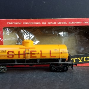 May include: A yellow toy train car with the word "SHELL" printed in red on the side. The car is labeled "SCCX 1260" and has a capacity of 8000 lbs. The car is part of a Tyco model train set.