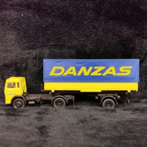 Puede incluir: Un camión de juguete amarillo con un remolque de lona azul. El remolque tiene la palabra "DANZAS" impresa en letras amarillas.
