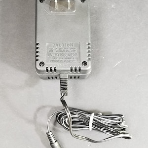 Pode incluir: Adaptador CA preto com um cabo de alimentação e um rótulo de advertência que diz "CAUTION RISK OF ELECTRIC SHOCK DRY LOCATION USE ONLY AVERTISSEMENT POUR UTILISATION A L'INTERIEUR SEULEMENT 0905".