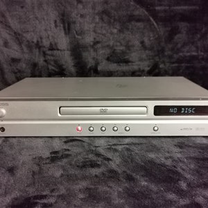 May include: A silver DVD player with a black display that reads "NO DISC". The player has a silver front panel with a slot for a DVD disc and several buttons.