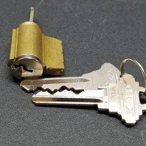 以下が含まれることがあります： 真鍮製のキーシリンダーと銀色のキー。キーには銀色のリングが付いています。キーには5125という番号が印刷されています。
