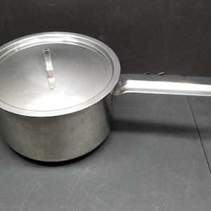 May include: A stainless steel pot with a lid and a handle. The pot is silver and has a shiny finish.