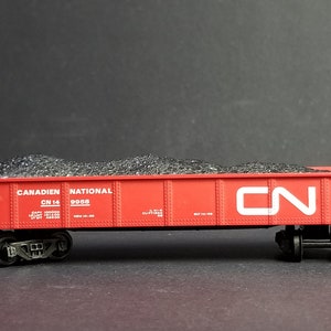 Peut inclure: Un wagon de train jouet rouge rempli de charbon noir. Le wagon est étiqueté "Canadien National" et "CN 14 9968".