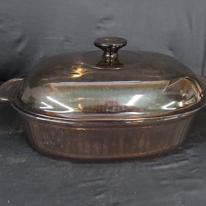 Puede incluir: Un plato para hornear de vidrio marrón con tapa. El plato tiene un diseño acanalado alrededor del borde.