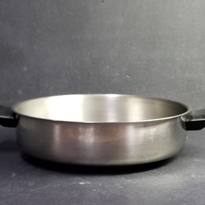 May include: A silver cooking pot with black handles. The pot is round and has a smooth surface.