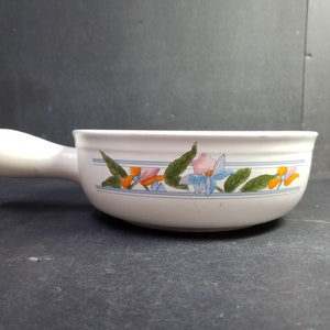 May include: White ceramic serving dish with a floral design in shades of blue, pink, orange, and green. The dish has a handle and is ideal for serving soup, dips, or sauces.