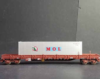 Op de afbeelding: Een rode en bruine modeltreinwagen met een witte container erop. De container heeft een groen en rood logo met een krokodil en het woord "MOL" in rode, blauwe en witte letters.
