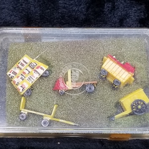 Puede incluir: Un conjunto de cinco vehículos de juguete en miniatura en una caja de plástico transparente. Los vehículos son amarillos y rojos, y son todos diferentes tipos de camiones. La caja está llena de un material moteado amarillo y blanco.
