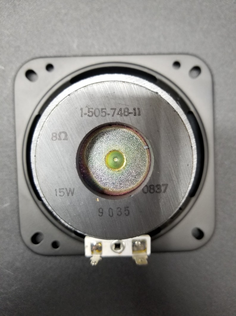 Pu&ograve; includere: Primo piano di un driver per altoparlanti con il numero di modello 1-505-748-11, 8 ohm, 15W e 9 035 stampato sul davanti. Il driver per altoparlanti &egrave; montato in una cornice di plastica nera.