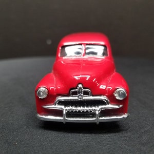 Può includere: Un modello di auto giocattolo vintage rosso con dettagli cromati. L'auto ha una parte anteriore arrotondata e un design classico.