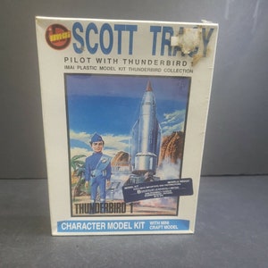 Puede incluir: Un kit de maqueta de plástico de Scott Tracy, el piloto de Thunderbird 1, de la clásica serie de televisión Thunderbirds. El arte de la caja presenta una ilustración colorida de Scott Tracy de pie frente a Thunderbird 1, que está despegando hacia el cielo. La caja también incluye el texto "Thunderbird 1" y "Character Model Kit".