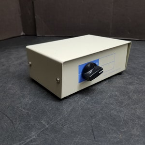 Puede incluir: Una caja blanca con una perilla negra y una etiqueta azul que dice "A".