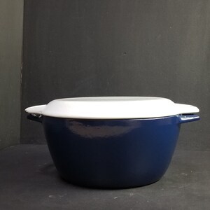 May include: A blue enamelled cast iron Dutch oven with a white lid. The oven has two handles on the sides and a single handle on the lid.