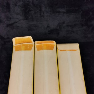 May include: Three white envelopes with yellow borders. The envelopes are folded in half and have a flap on the top. The envelopes are all the same size.