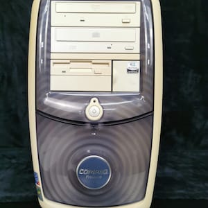 May include: A beige desktop computer tower with a clear plastic front panel. The front panel has a CD-ROM drive, a floppy disk drive, and a power button. The computer is labeled "Compaq Presario 5000".