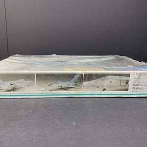May include: A plastic model kit of a grey F-14 Tomcat fighter jet. The box shows three different views of the plane, including the top, side, and front. The box is labelled "F-14 Tomcat" and "1/72 Scale".