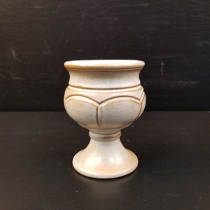 Puede incluir: Un cáliz de cerámica blanca con un borde y una base marrones. El cáliz tiene un diseño acanalado y una base de pedestal.