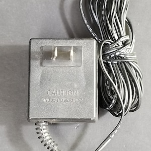 May include: Black power adapter with a black cord and a two-prong plug. The adapter has the text "CAUTION" and "INDOOR USE ONLY" printed on it.